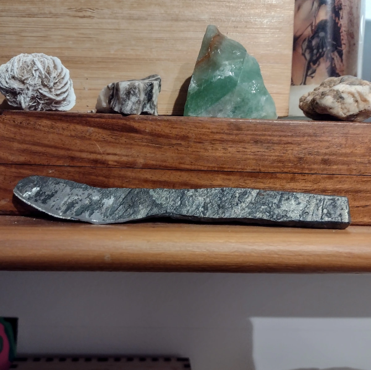 A rough hand-forged iron butter knife displayed on a red ceder shelf along with several small mineral-rocks.