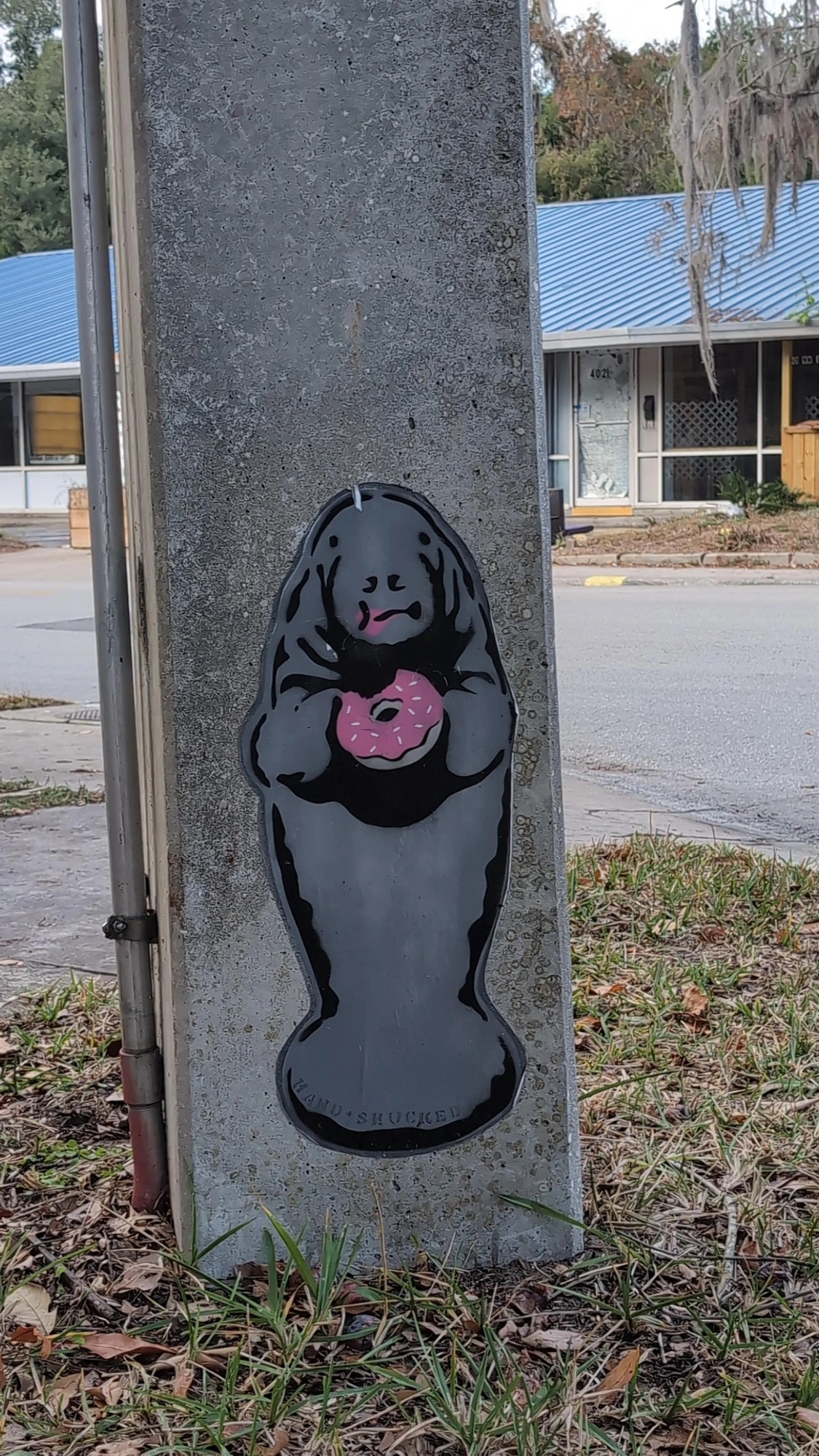 A stenciled image of a manatee holding a donut with a bite taken out of it, spray painted on a concrete utility pole.