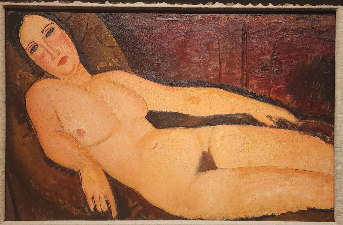 nude woman reclining on red divan, looking at viewer.