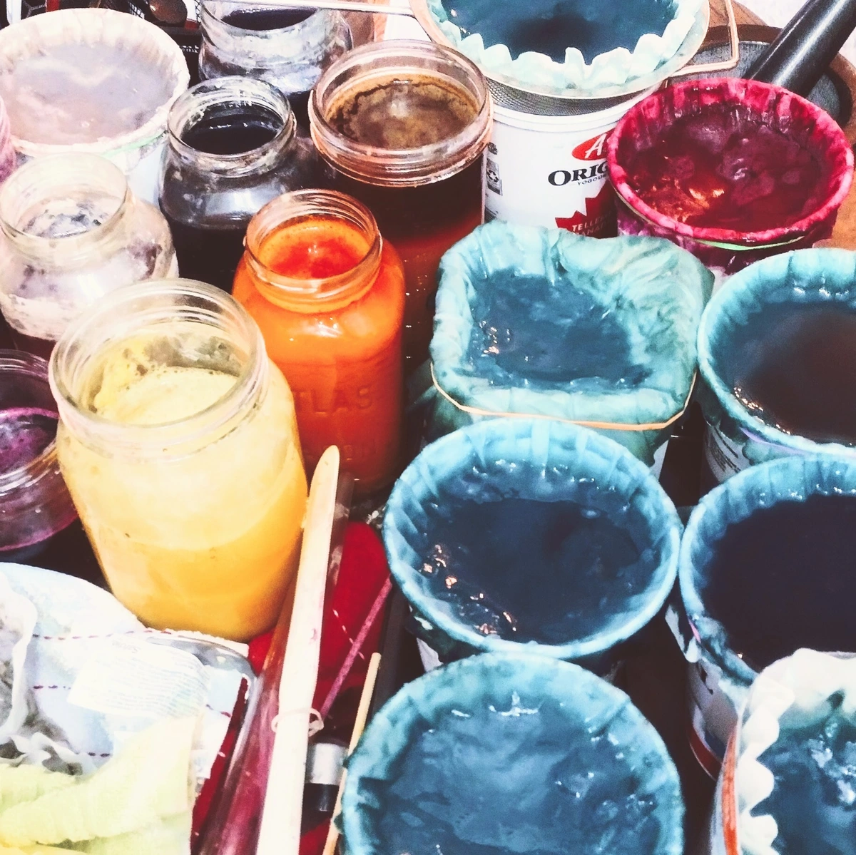 Image of crowded jars with coffee filters tied over the tops, filled with wet, filtering pigments in blues, reds, oranges and browns.