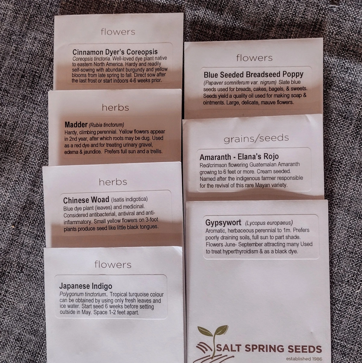 Seven paper packages of seeds arranged on a table.