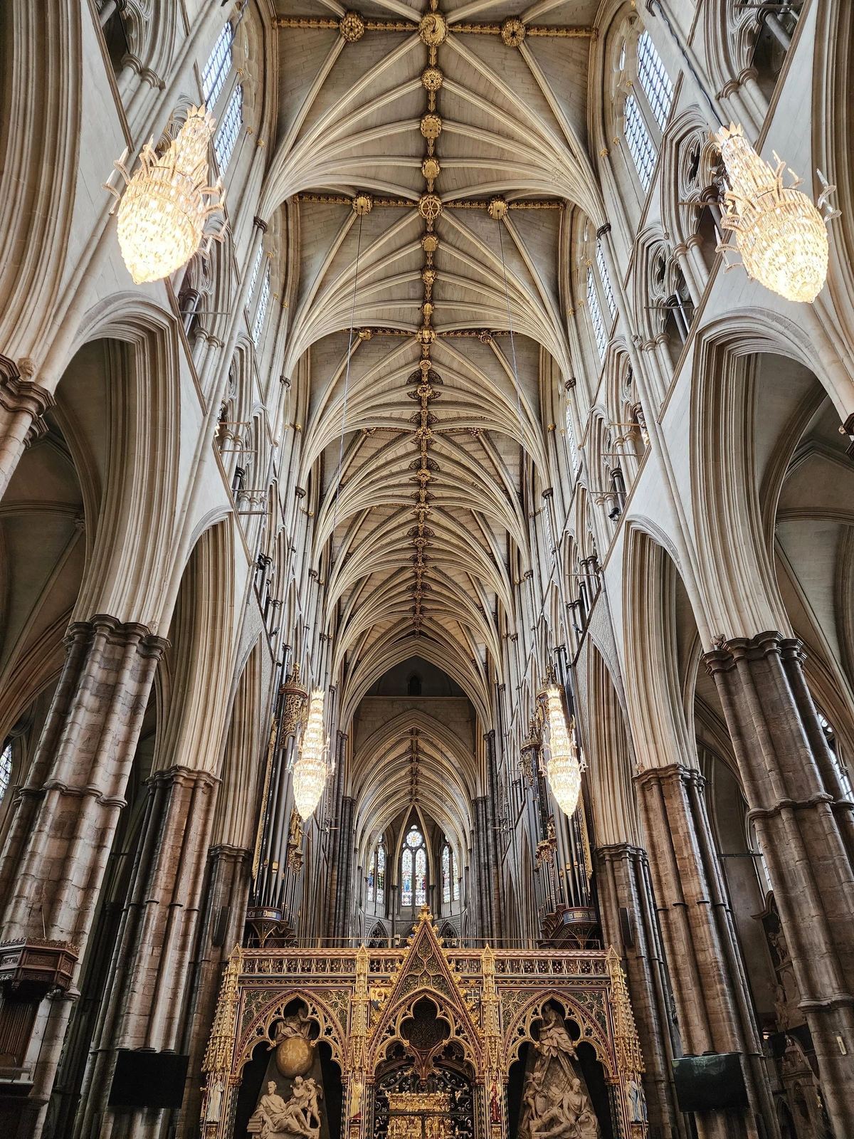 looking up at the ceiling from one end of the church with the apse at the opposite end. the church is very tall and narrow, and the ceiling is composed of ribbed vaultings that emerge from a central ("spine") ribbing and join in fours to form the columns of the upper walls. in foreground spanning the bottom length of the nave is the top of an ornate wooden rood screen.
